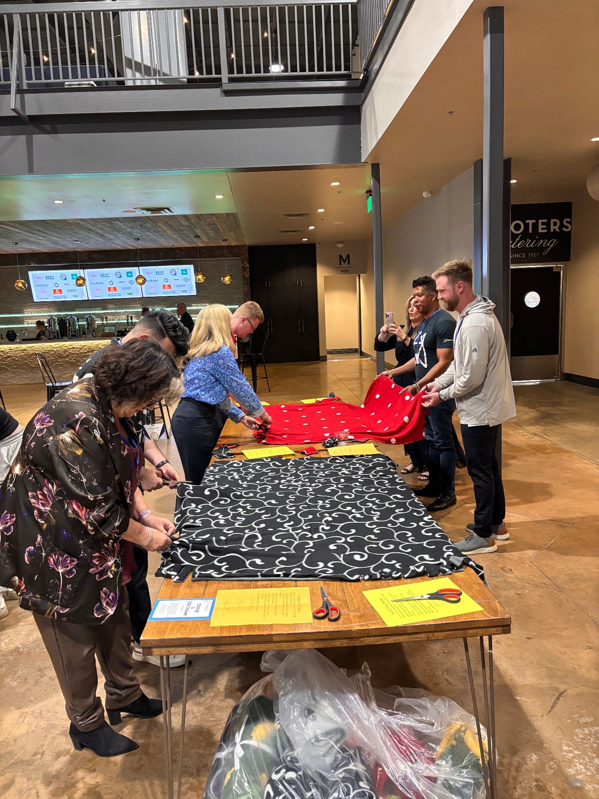 Hosts gathered around tables making no-sew blankets together at a hospitality event